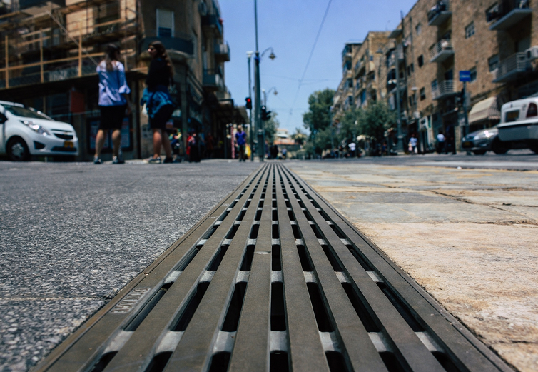 Close-up of a sewer grate in an urban street with pedestrians